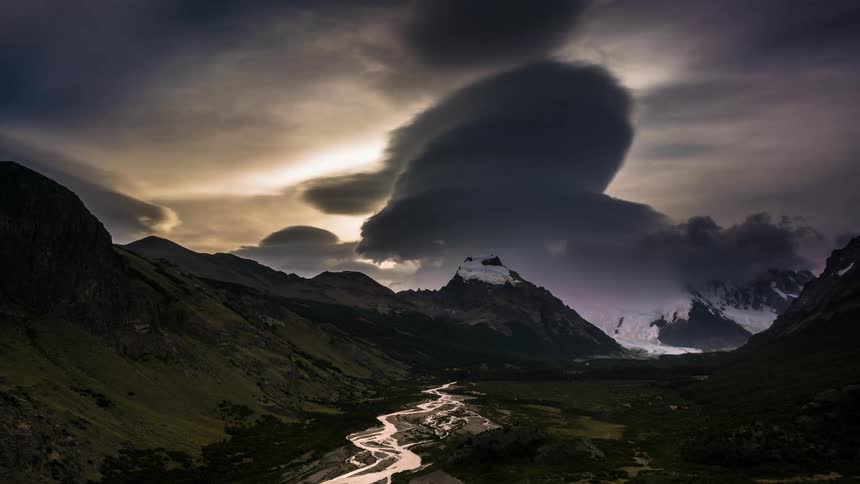 Landscape of a mountain valley with snow and clouds passing by and the sky changing shades