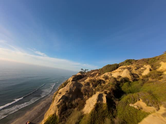 A view of a rugged coastline with a steep cliff dropping down to a sandy beach and the vast ocean beyond