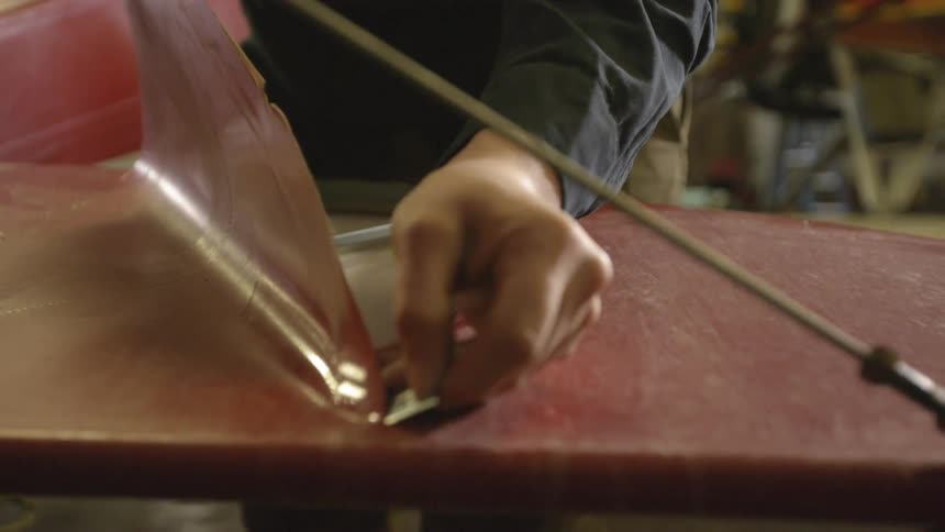 Man removing a layer from a piece of furniture using a razor blade