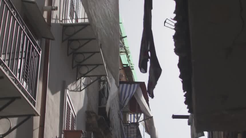 A narrow winding alleyway in a european city lined with tall buildings and balconies filled with laundry drying in the sun