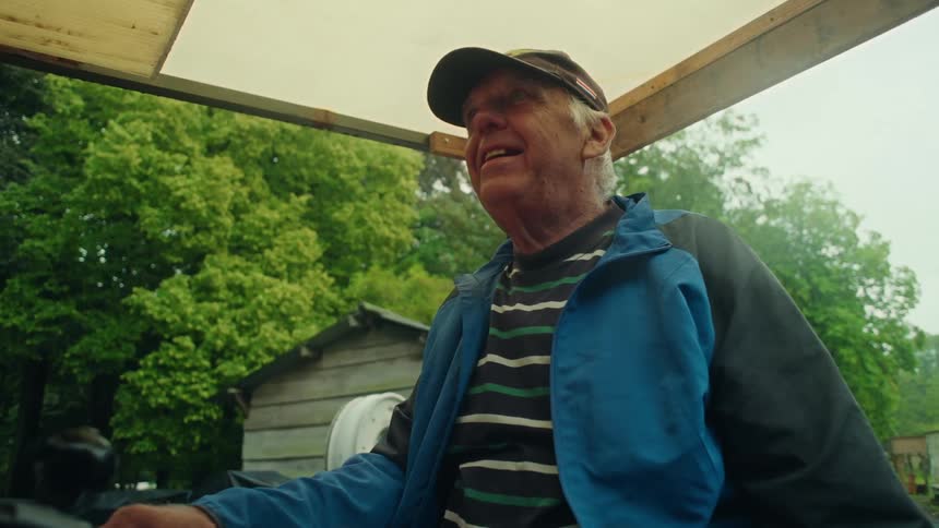 An elderly man with blue and black jacket looking down with a small smile on his face then he looks forward