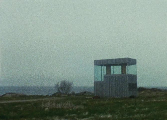 A small building with the top surrounded by glass windows in a field of grass