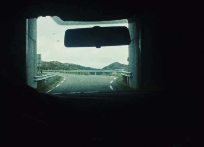 A person driving a car through a tunnel onto a highway running by mountainous terrain