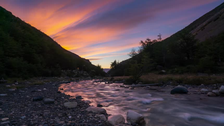 A stream with several rocks on the sides in a fast movement and with the orange sky where it is getting day