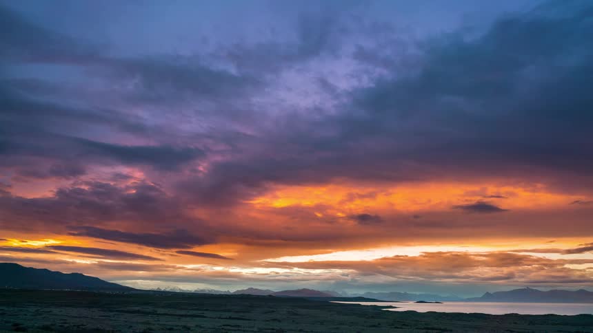 A sunset with fiery orange and purple clouds casting a warm glow over a vast desert landscape