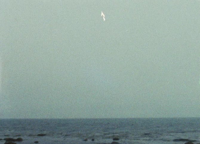 A calm misty sea with a faint coastline in the distance creating a serene and atmospheric scene