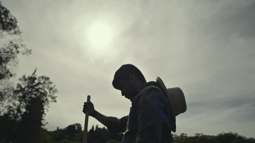Man holding a wooden rod while standing in a natural setting on a cloudy day
