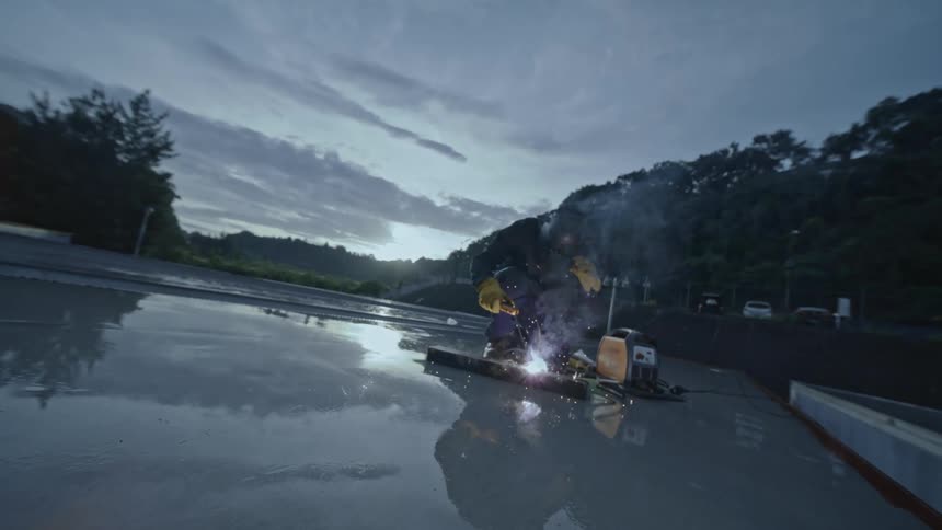 A worker welds on a slick looking surface outdoors at dusk