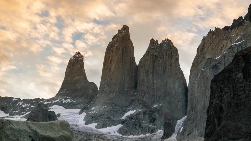 Dark clouds float over a series of large mountains partially covered in snow