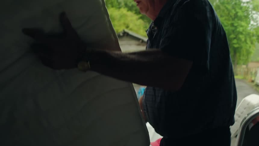 An old man moves a mattress into the back of a truck