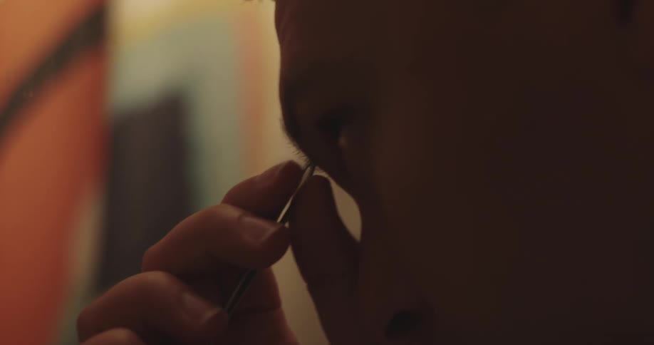 Close up of a mans face doing his eyebrows in front of the mirror