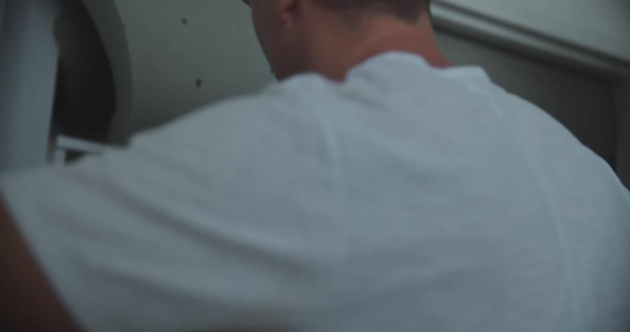 The man in the white shirt is putting a dark outfit inside a closet and closing the door