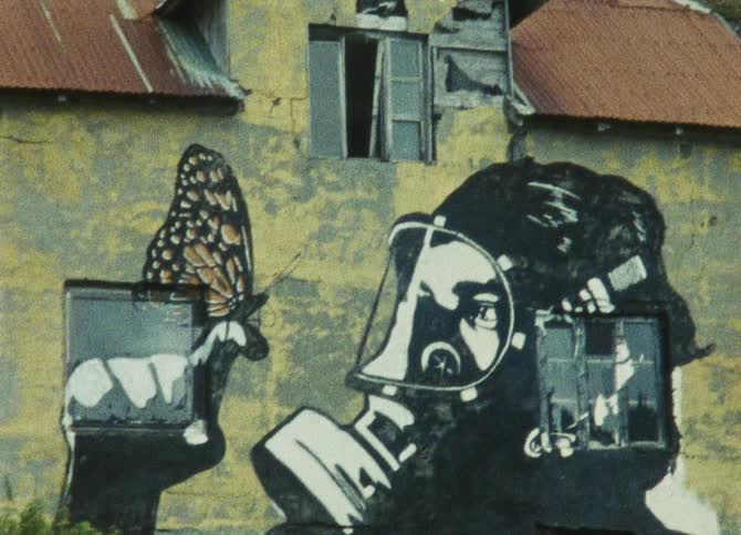 A graffiti mural of a person wearing a gas mask is painted on the side of a building