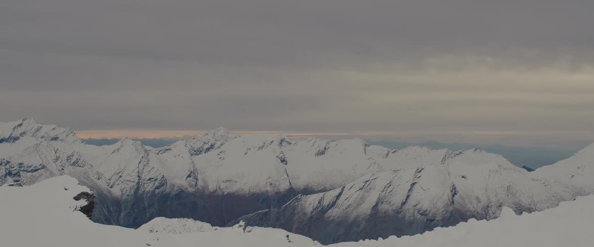 Dark clouds hang over a mountain range covered in snow