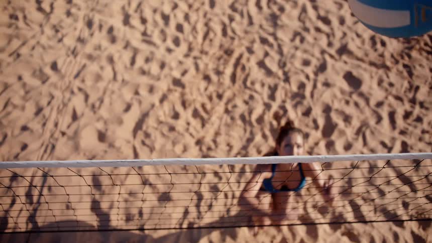 A woman jumping to hit a volleyball that went over a net on a sand volleyball court