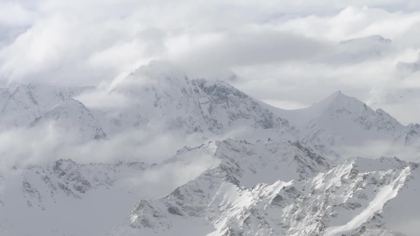 Clouds cover the top of snowy mountain peaks