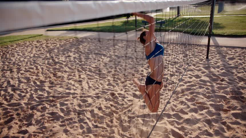 Woman jumping and playing volleyball on a sand court