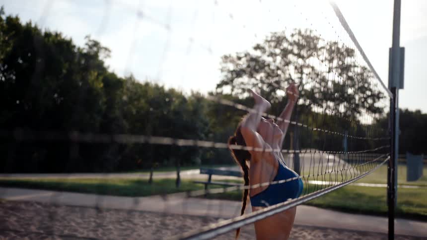 Woman jumping and throwing a ball on a sand volleyball court