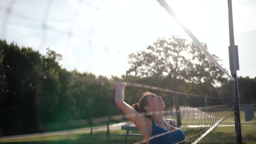 Woman jumping and hitting a volleyball while playing on an openair sand court