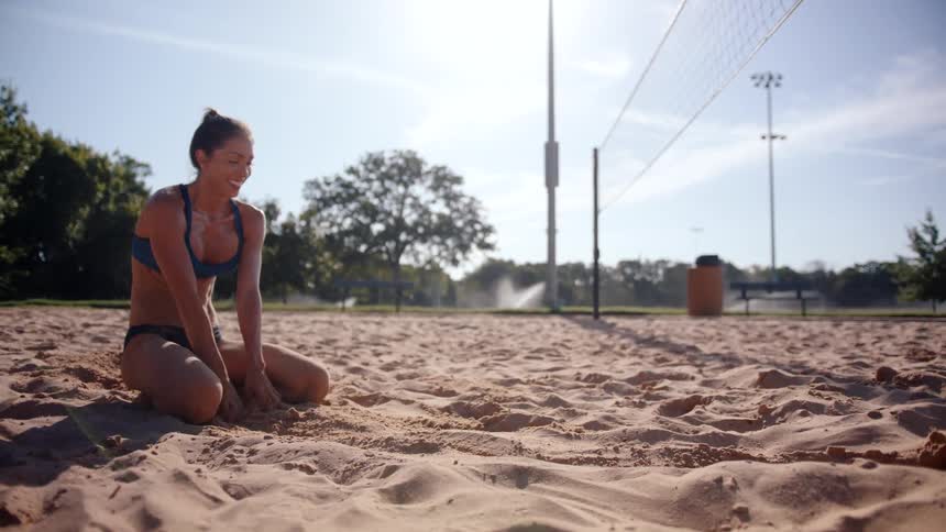 Woman kneeling in the sand on a volleyball court smiling