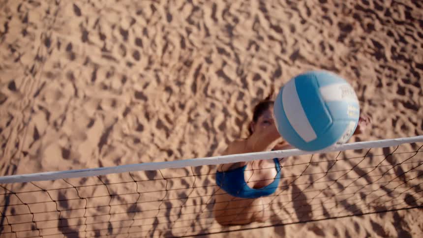 Woman jumping and hitting a volleyball in a match on a sand court