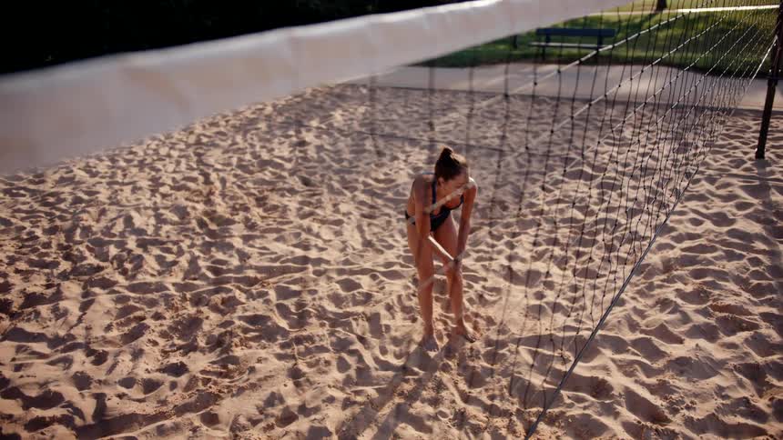 A female volleyball player prepares for an upcoming match by sanding her hands on a sandy beach court