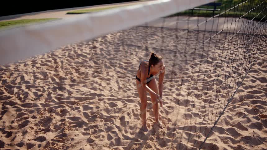 A woman in summer clothes is rubbing her hands and she is on a sand volleyball court