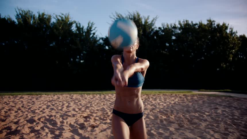 Woman in bikini on a sand court hitting volleyball