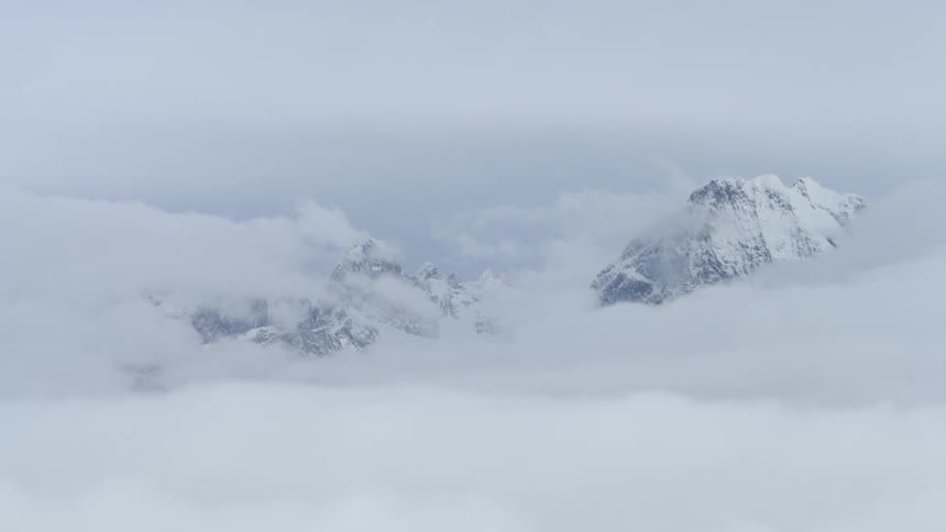 Clouds hover just below the peak of a tall mountain covered with snow
