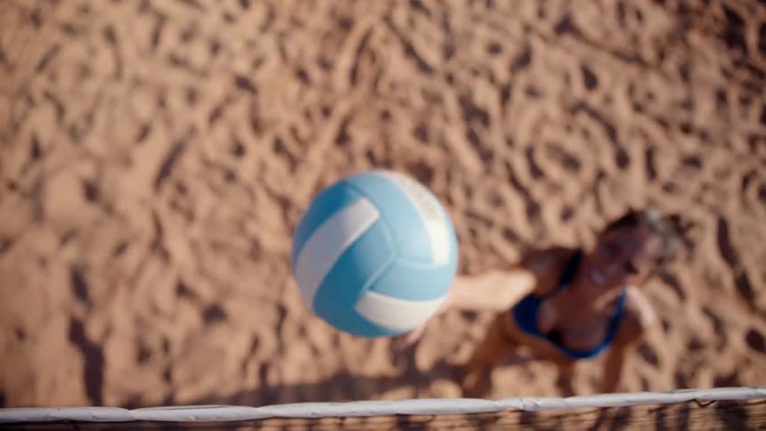 A woman standing on a sand court during a beach volleyball game throws the ball up
