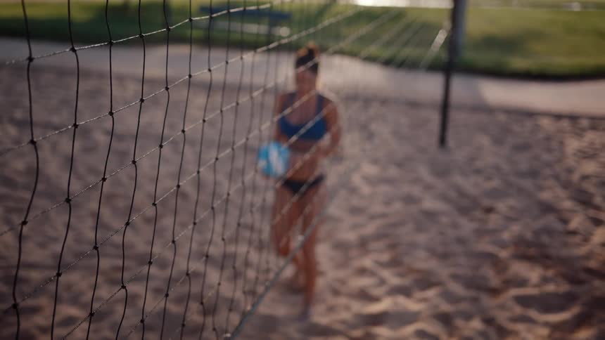 Woman entering a sand court with a volleyball