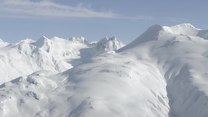 Snow covers the peaks of a tall mountain range under a blue sky