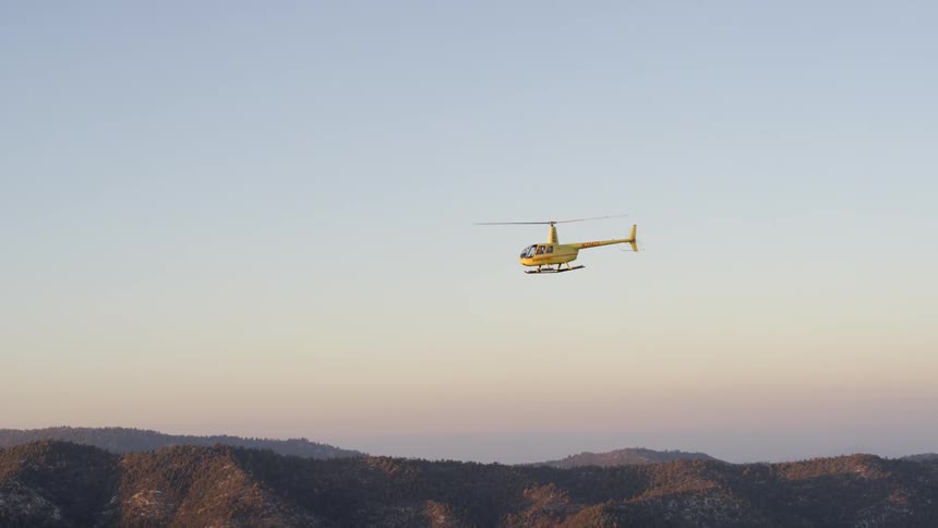 A yellow helicopter being filmed in the distance from the air