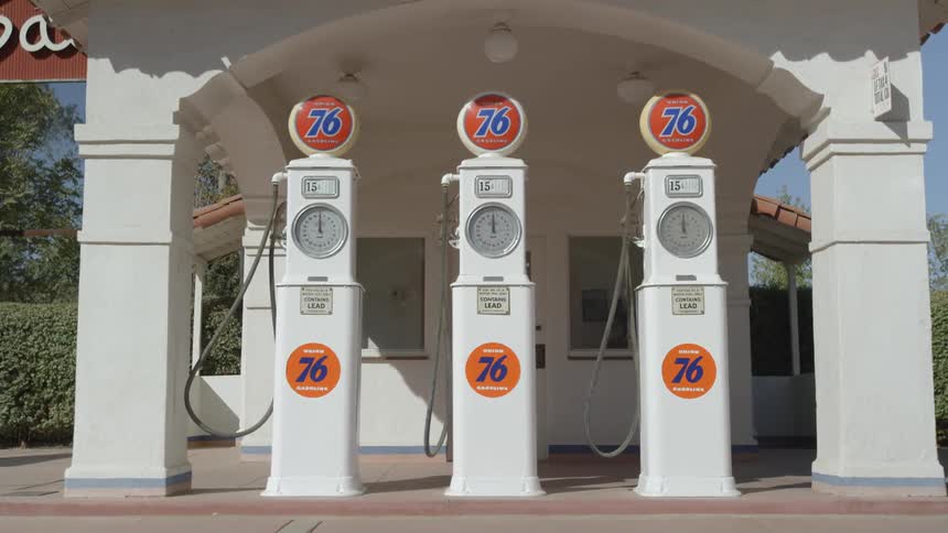 A gas station has an orange sign with the number seventy six