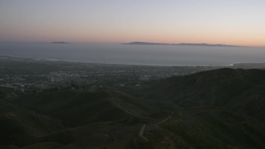 Dusk is settling over the ocean beyond hills and a community
