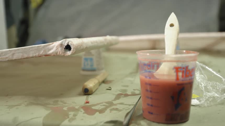 Paintbrush in some reddish liquid  with a person working in the background