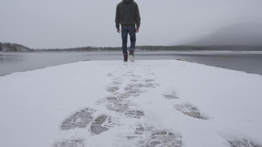 Man walks on a snowy area close to water