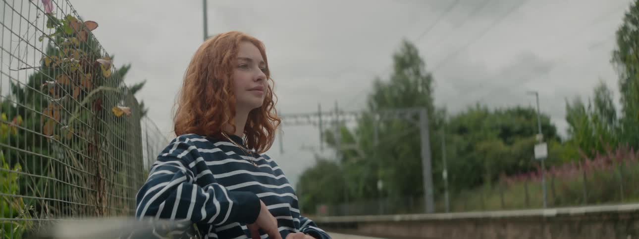 Redheaded woman sitting on a bench in an open air environment on a cloudy day