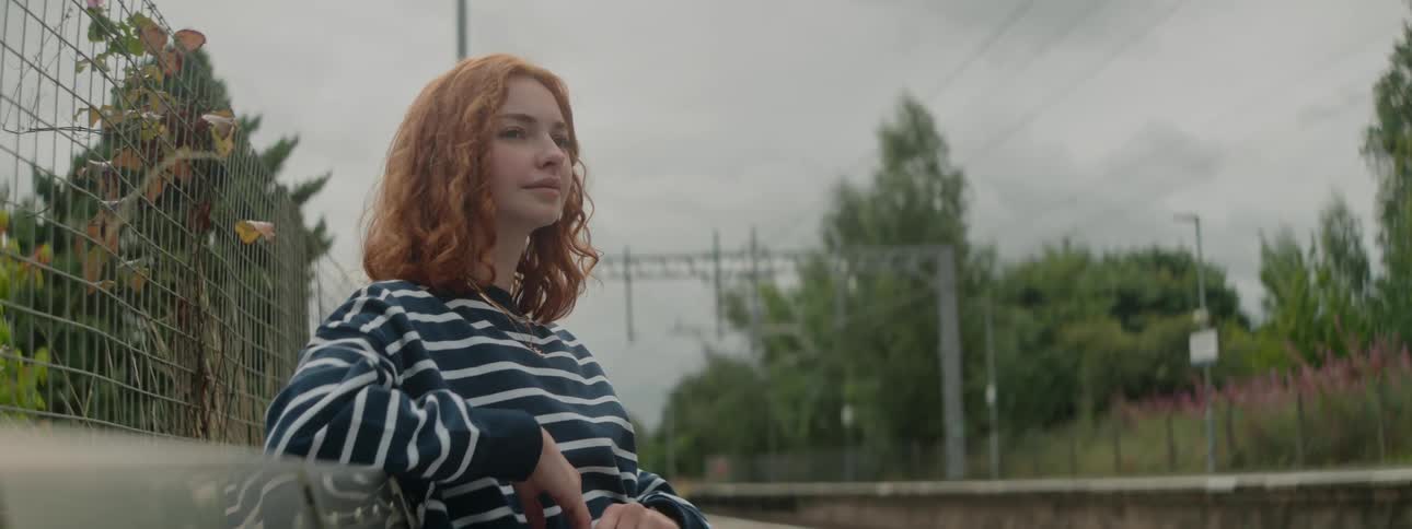 A redhead woman in a striped sweater sits on a bench on an empty street