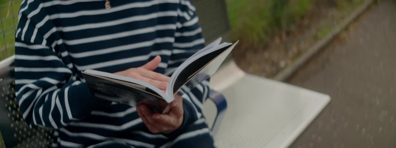 Person sitting on an openair bench reading a book