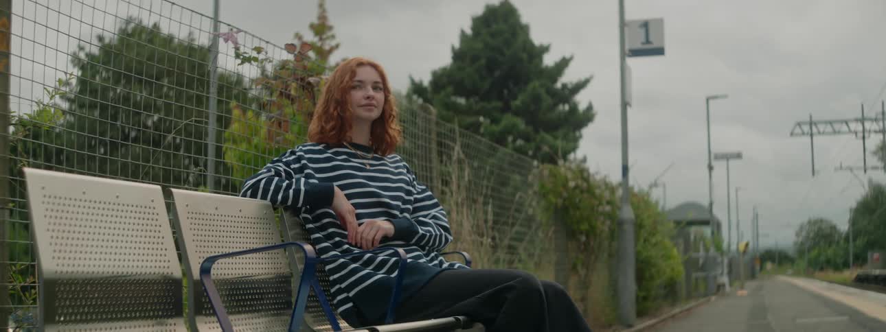 Redheaded woman sitting on a bench near empty railroad tracks looks around