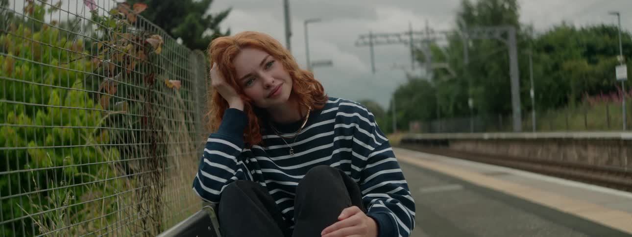 Redheaded woman sitting next to a train track in an outdoor area