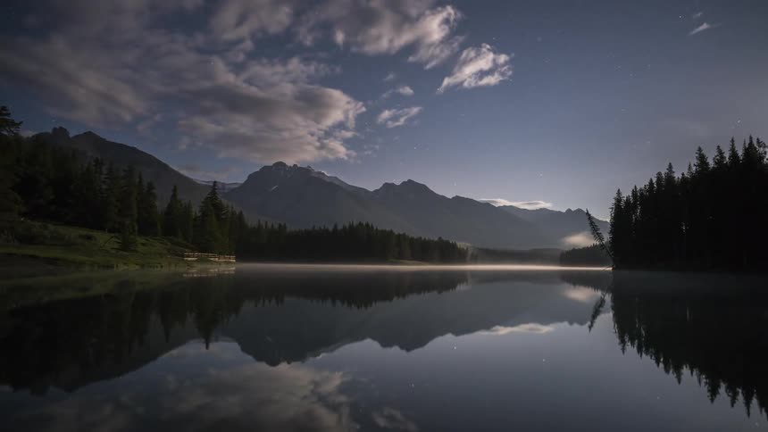 Clouds move over a lake and mountain range in a rural area
