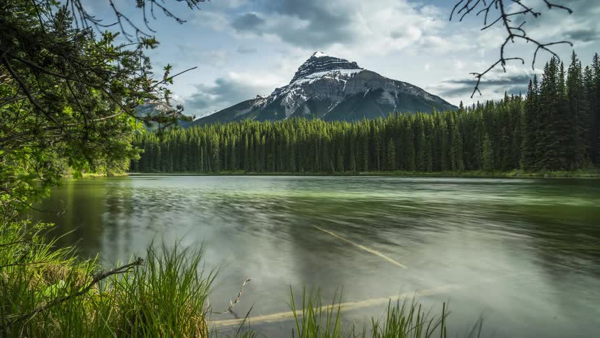 Clouds pass above a natural landscape with a lake coniferous forest and mountains in the background
