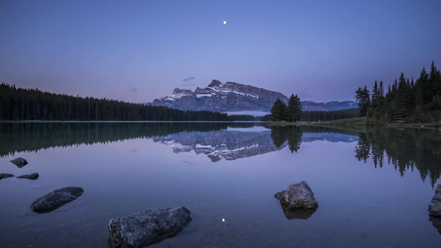 The sun moves across the sky at dusk over a mountain and a lake
