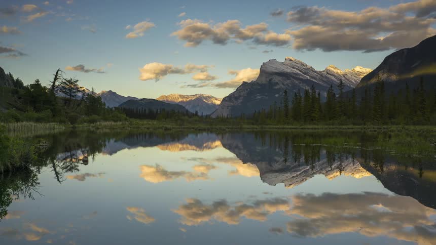 Lake reflects the passing clouds and the nearby mountains as the sun sets
