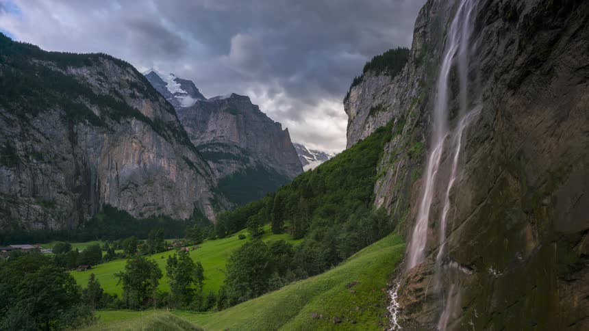 A waterfall flows down a mountain face into the valley below