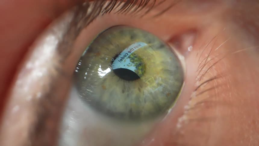 Eye of a white person reflecting the light and images on a screen in front of them