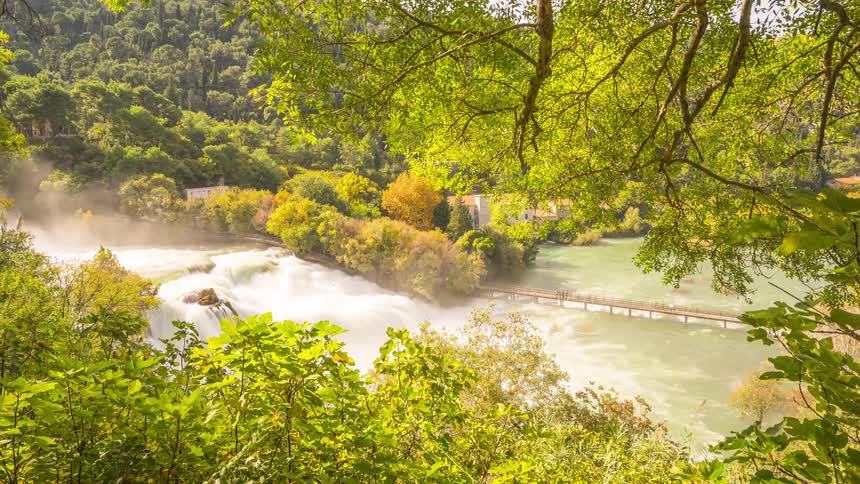 Natural scenery of a bridge with tourists crossing a waterfall with a deep river surrounded by vegetation