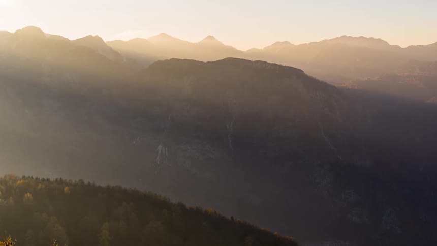 A mountainous region with a green hill in front and there are strong sunlights coming from the right